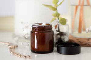 Jar of natural, organic skin cream next to a medicinal plant